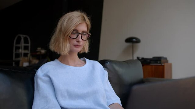 Blonde woman portrait in eyeglasses with tense emotions, concentrated on her job. Stylish adult person looking at the screen, typing. Concept of freelancer