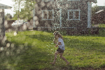 kid running in cool water splash in backyard, watering garden