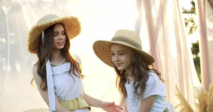 Two cheerful brunette girls with long hair in straw hat smiling and posing to the camera