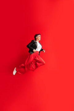 Stylish woman in trousers jumping on red background