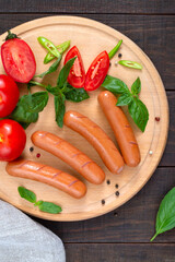 Delicious spicy hot dog sausages with fresh tomatoes and basil on a cutting board. Sausages for breakfast. Top view.