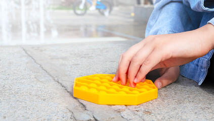 Child with Pop It game playing outdoors. Kid hands playing with silicone antistress fidget toy, close up. Copy space