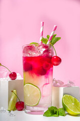 Cold and refreshing summer drink. Cherry cola, limeade, mojito lemonade cocktail with lime and cherries on colorful bright pink background