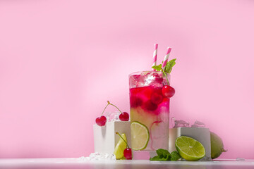 Cold and refreshing summer drink. Cherry cola, limeade, mojito lemonade cocktail with lime and cherries on colorful bright pink background