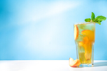 Cold and refreshing summer drink. Classic iced peach tea cocktail with fruit slices on colorful bright blue background