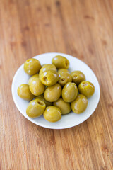 Pickled stuffed green olives on a white plate set on wooden kitchen board close up shot top view