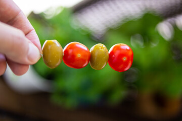 Pickled stuffed green olives and fresh red cherry tomatoes on a skewer held in hand by male hand close up shot shallow depth of field