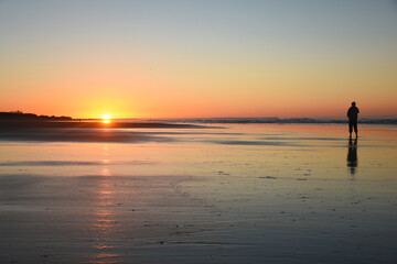 Man watching the sunrise on the beach, with warm tones and a beautiful reflection of the sunlight in the water