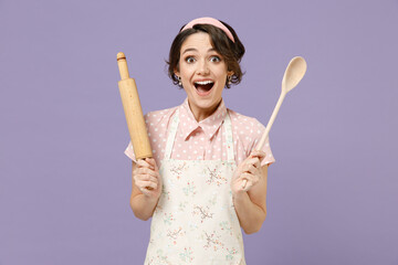 Young surprised fun exicted amazed impressed housewife housekeeper chef cook baker woman in pink apron hold wooden spoon rolling pin isolated on pastel violet background Cooking food process concept