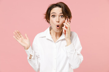 Happy surprised young employee business woman corporate lawyer in classic formal white shirt work in office talk by mobile cell phone spread hands isolated on pastel pink background studio portrait.