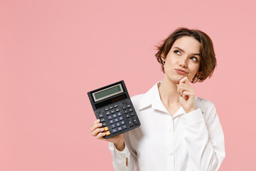 Young dreamful successful employee business secretary woman corporate lawyer in classic formal white shirt work in office hold in hands calculator isolated on pastel pink background studio portrait - obrazy, fototapety, plakaty