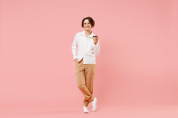 Fototapeta na wymiar Full length young employee business woman corporate lawyer in classic formal white shirt work in office hold takeaway delivery craft paper brown cup coffee to go isolated on pastel pink background