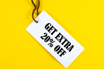 GET EXTRA 20 OFF percent text on a white tag on a yellow paper background