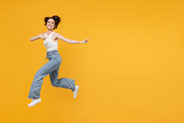 Fototapeta na wymiar Full length young fun happy excited woman 20s with bob haircut wearing white tank top shirt jumping high point index finger aside on copy space area mock up workspace isolated on yellow background