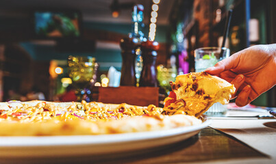 woman Hand takes a slice of meat Pizza with Mozzarella cheese, salami, pepper, ham in cafe