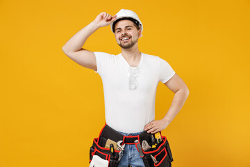 Young smiling happy employee handyman man in protective helmet white t-shirt tipping hardhat isolated on yellow background. Instruments accessories for renovation apartment room. Repair home concept.