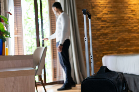 Male tourist with suitcase opening door in hotel room