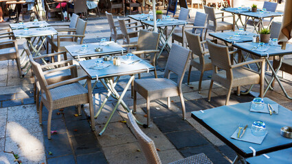 Outdoor cafe terrace with empty tables, wicker chairs on a bright sunny day