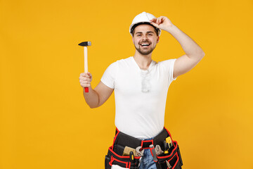 Young smiling employee handyman man in protective helmet glasses hold hammer tipping hardhat isolated on yellow background studio Instruments accessories renovation apartment room Repair home concept.