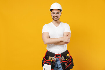 Young employee handyman man in protective helmet hardhat glasses hold hands crossed isolated on yellow background studio portrait Instruments accessories renovation apartment room Repair home concept