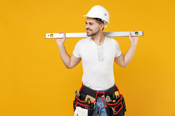 Young employee handyman man in protective helmet hardhat hold build bubble spirit level look aside isolated on yellow background Instruments accessories renovation apartment room Repair home concept.