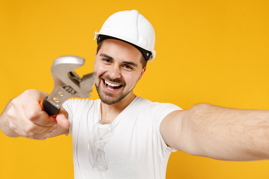 Young employee handyman man in protective helmet hardhat give adjustable wrench do selfie mobile phone isolated on yellow background Instrument accessories renovation apartment room Repair concept