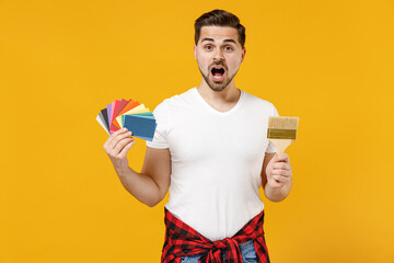 Young shocked employee handyman man wear t-shirt hold color palette paint brush isolated on yellow background studio portrait Instruments accessories for renovation apartment room Repair home concept