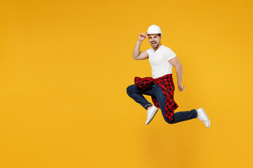 Fototapeta na wymiar Full length side view young employee handyman man 20s wearing protective helmet jump high run isolated on yellow background. Instruments accessories for renovation apartment room. Repair home concept.