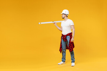 Full length young fun employee handyman man in protective helmet hold build bubble spirit level walk go isolated on yellow background Instruments accessories renovation apartment room Repair concept.