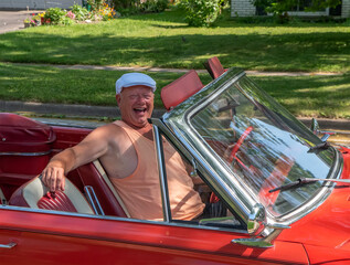 A very happy man with big smile driving his old, vintage 1960s red convertible.