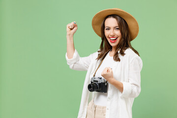 Traveler tourist woman in casual clothes hat camera on neck clench fist do winner gesture say yes isolated on green background. Passenger travel abroad on weekends getaway Air flight journey concept - obrazy, fototapety, plakaty