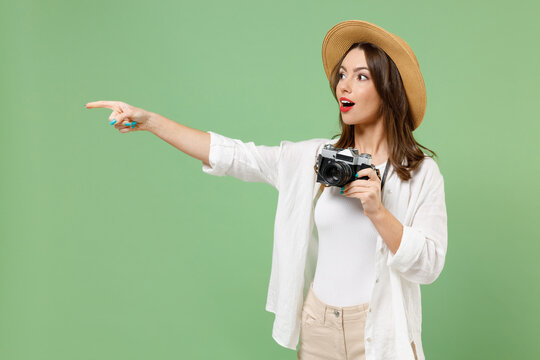 Fun traveler tourist woman in casual clothes hat take picture on retro photo camera point figer aside isolated on green background Passenger travel abroad weekends getaway Air flight journey concept