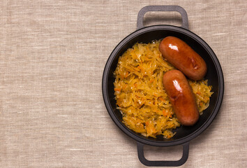 Appetizing delicious sausages and stewed cabbage in a frying pan - a traditional dish of German, Polish or Russian cuisine. Top view.