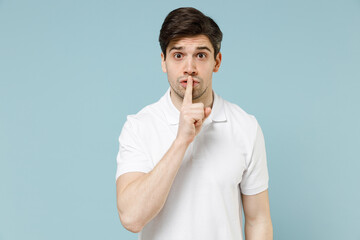 Young secret unshaven man 20s wearing white casual basic t-shirt say hush be quiet with finger on...