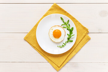 Fried eggs with arugula in a plate on a yellow linen napkin. Horizontal orientation, top view.
