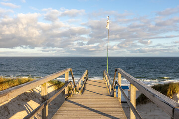 Obraz premium a wooden footbridge that leads over a dune directly to the sea. Viewpoint of a staircase over the blue sea and sky. 