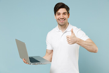 Young happy man in white casual basic t-shirt hold laptop pc computer chat online browsing internet...