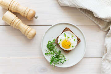 Toast with fried egg, onion and arugula in a plate on a wooden table. Horizontal orientation, top view.
