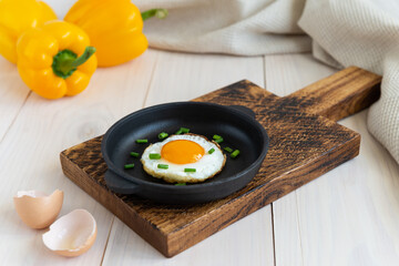 Fried egg with green onions in a cast-iron pan with bell peppers on a wooden table.