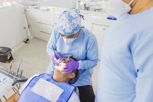 Unrecognizable dental hygienist cleaning teeth of patient in clinic