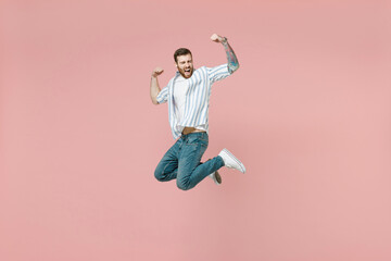 Full length young overjoyed unshaven man 20s in blue striped shirt white t-shirt jump high do winner gesture clench fist isolated on pastel pink background studio portrait. People lifestyle concept.