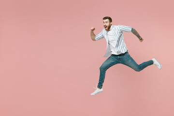 Fototapeta na wymiar Full length side view sporty young caucasian unshaven man 20s wearing blue striped shirt white t-shirt jump high run fast hurry up isolated on pastel pink color background. People lifestyle concept.