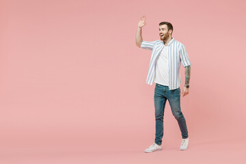 Fototapeta na wymiar Full length young happy smiling friendly caucasian unshaven man 20s in blue striped shirt walking going waving hand isolated on pastel pink color background studio portrait. People lifestyle concept.