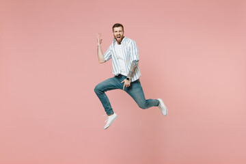 Fototapeta na wymiar Full length young overjoyed musician unshaven man 20s wear blue striped shirt white t-shirt jump high playing guitar gesture isolated on pastel pink background studio portrait. Tattoo translate fun