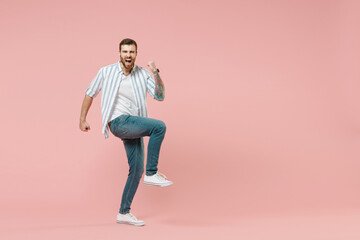 Fototapeta na wymiar Full length young fun overjoyed caucasian unshaven man 20s in blue striped shirt clench fist do winner gesture with raised up leg isolated on pastel pink background studio. People lifestyle concept.