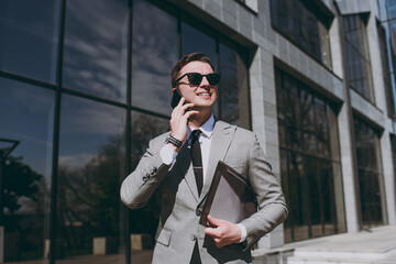 Young employee business man 20s in grey suit walk go near office glass wall building outdoors in...