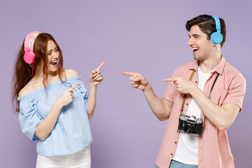 Two traveler tourist woman man couple in shirt colorful headphones listen to music point finger to each other isolated on purple background Passenger travel abroad weekends getaway Air flight concept.
