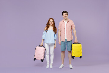 Full length two smiling happy fun traveler tourist woman man couple in shirt holding suitcase isolated on purple background. Passenger travel abroad on weekends getaway. Air flight journey concept