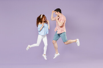 Fototapeta na wymiar Full length traveler tourist woman man couple in shirt do winner gesture clench fist jump high isolated on purple background. Passenger travel abroad on weekends getaway. Air flight journey concept.