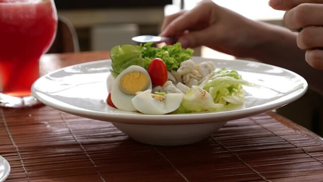 Woman cut boiled egg with table-knife, start eating fish salad, close up shot of served meal on bowl plate with wide edge. Light food served at restaurant as dinner starter